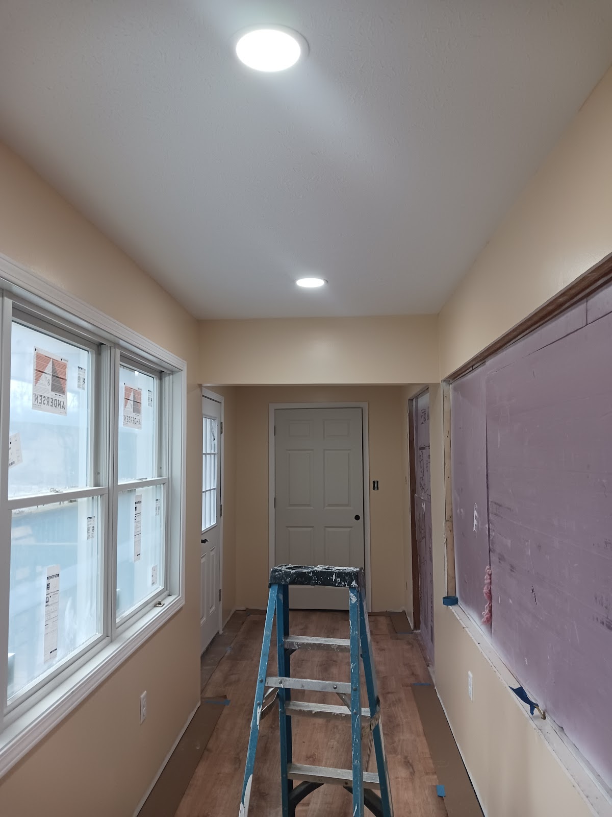 New recessed can lighting installed during a home renovation, with windows still filmed in plastic